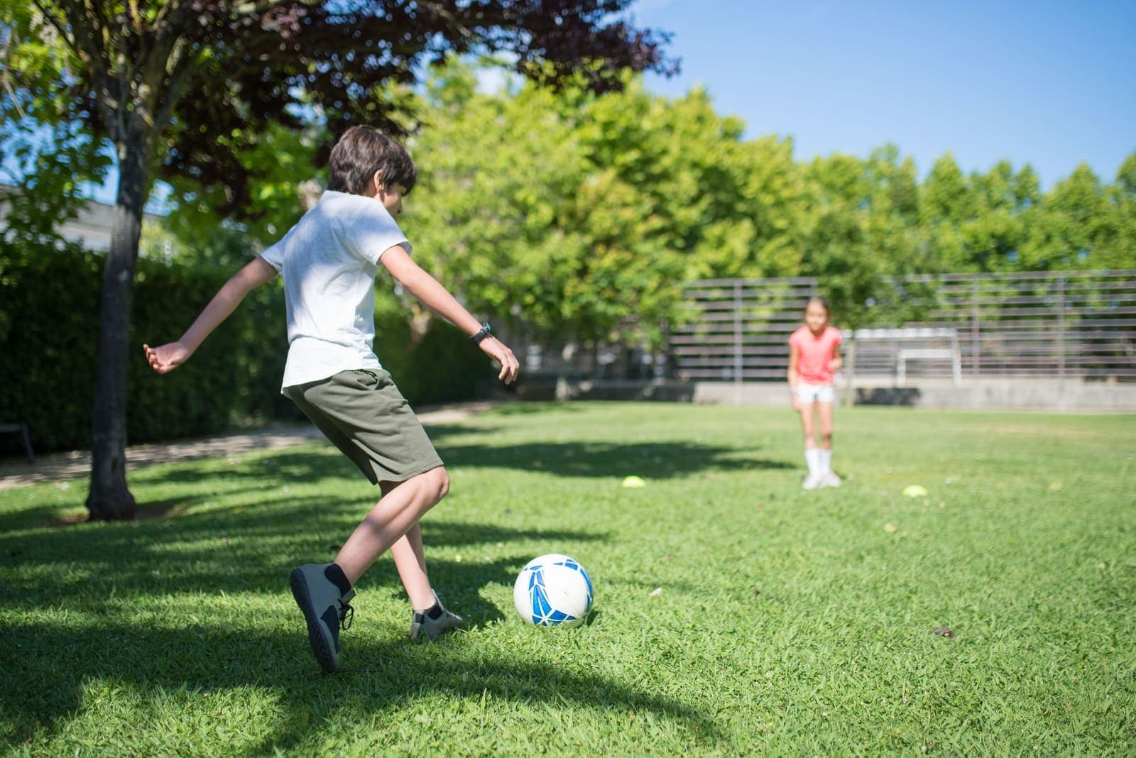 A young player kicking a football in a sunny park
