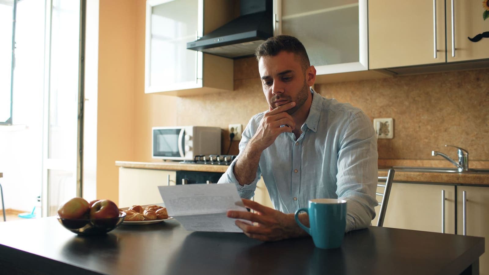 A young man reading a letter at a kitchen table